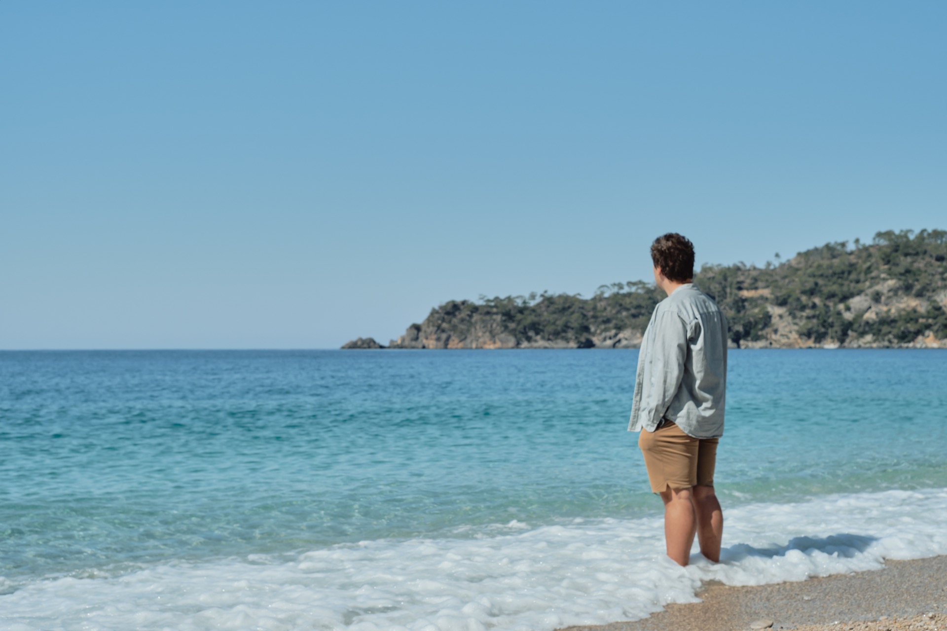 A man standing in the surf, looking out to sea